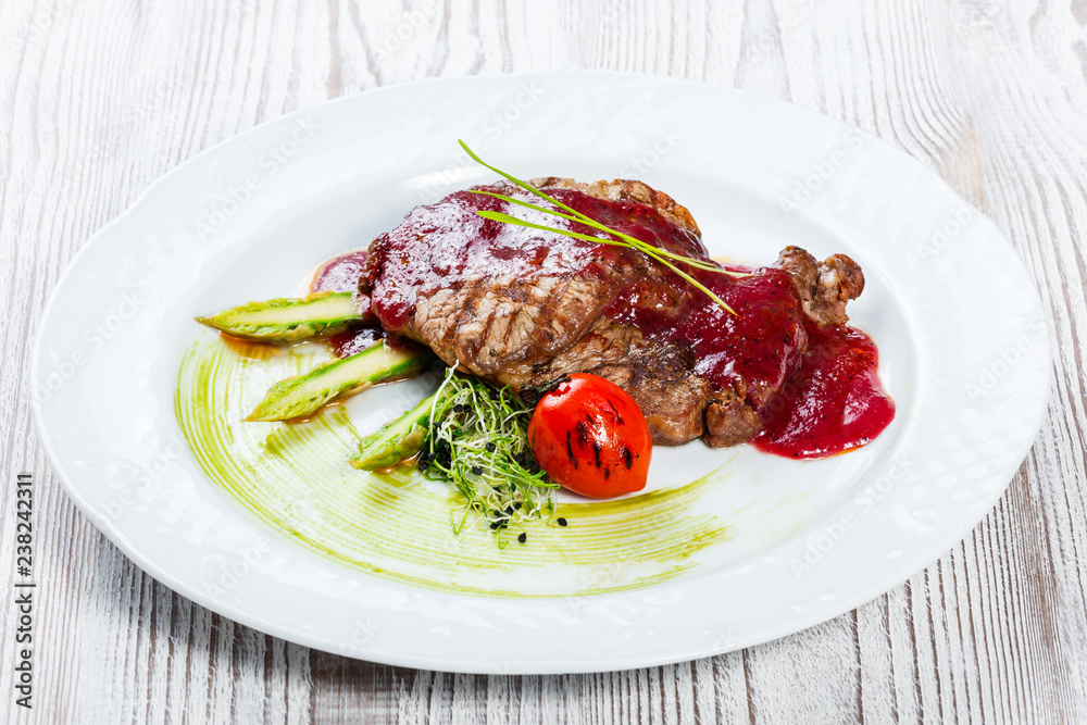 Grilled ribeye beef steak with berry sauce, asparagus and broccoli on light wooden background. Hot Meat Dishes. Top view, flat lay