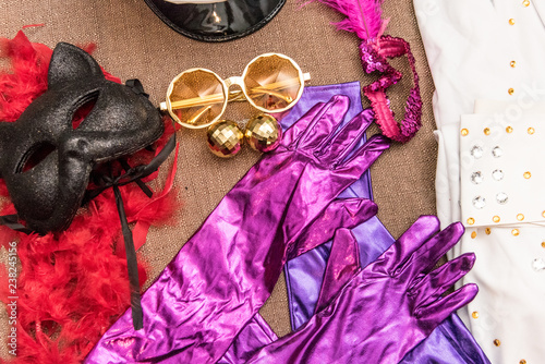 elementos de disfráz colorido, lentes dorados, plumas rojas y guantes morados para fiesta
