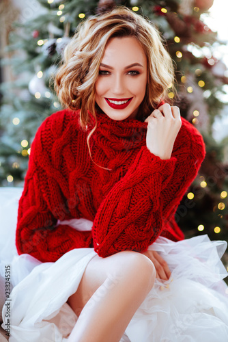 holidays, celebration and people concept - smiling woman in red sweater over christmas tree background