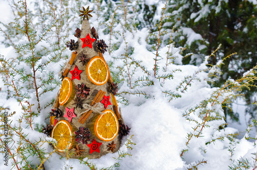 Необычная новогодняя ель, выполненная в стиле «арт-деко» украшенная сушеными апельсинами, сосновыми шишками и корицей на фоне заснеженной хвои. photo
