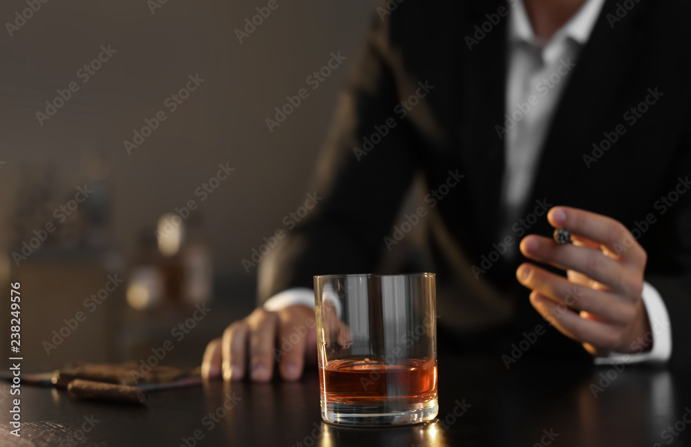 Man with glass of whiskey and cigar sitting at table, closeup. Space for text