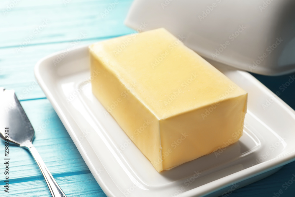 Dish with fresh butter and knife on wooden background, closeup Dish with fresh butter and knife on wooden background, closeup