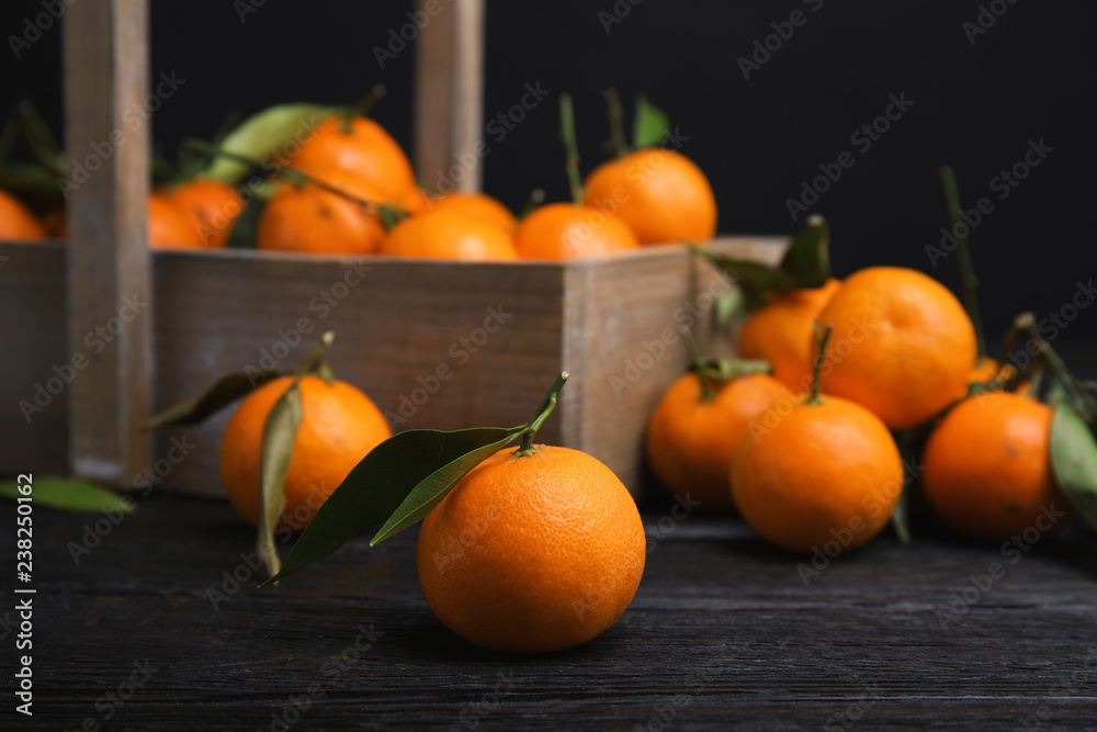 Fresh ripe tangerines with green leaves and wooden basket on table