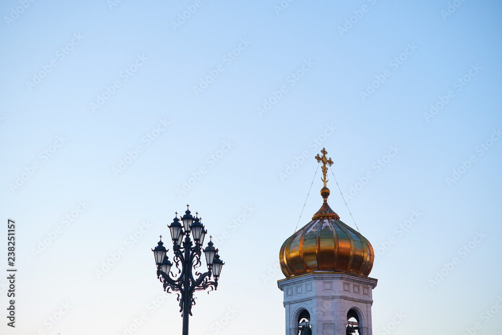 A golden dome and a cross of a chirch with a street lamp with blue sky on the background