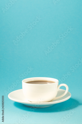 white cup on a blue background/white cup with a saucer full of black coffee on a blue background with copyspace