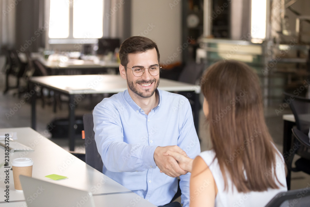 Obraz premium Friendly smiling employee shaking hand with young woman, newly hired office worker meeting with female colleague, first day at work, applicant, intern, trainee at job interview with employer, mentor