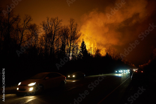 Forest fire with smoke and a road with cars at night, view from the distance
