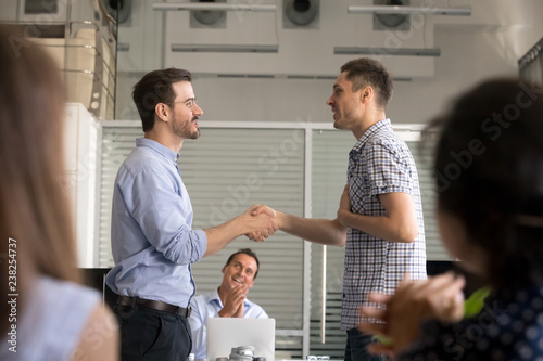 Team leader motivating handshaking male employee, congratulate with promotion, business achievement, ceo shaking hand, thank for good result, work, expressing respect, support, colleagues applaud