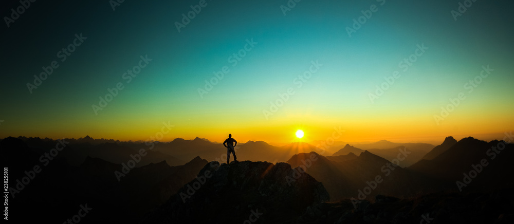 Man reaching summit enjoying freedom and looking towards mountains sunrise. - obrazy, fototapety, plakaty 