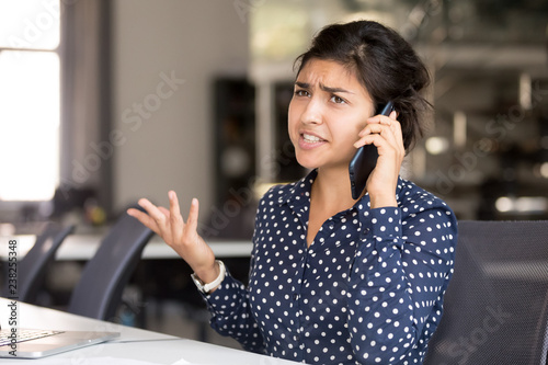 Outraged attractive Indian female employee talking by phone, arguing with client or customer, actively gesticulating, businesswoman having serious conversation on smartphone, solve business problem