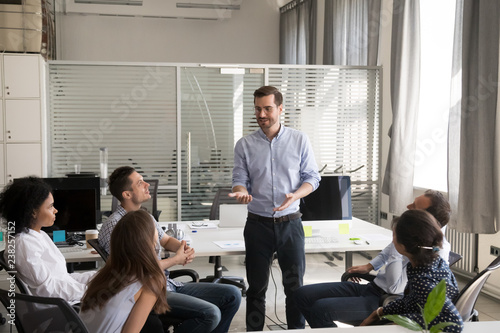 Confident male leader, coach holding briefing for multiracial team employees in office, discussing, explaining business strategy, plan to subordinates, businessman at company meeting with colleagues