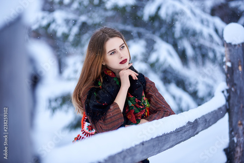 Portrait of attractive young female with long straight loose hair in long woolen stylish dress and dark kerchief with bright floral pattern outdoors i on sunny snowy winter day. photo