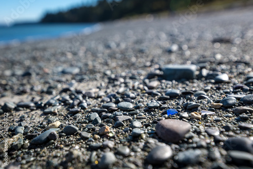 Rare bright blue colored sea glass on the beach amongst pebbles and sand. Possible concept image for standing out from the crowd and being yourself.