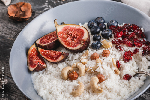 Rice coconut porridge with figs, berries, nuts, dried apricots and coconut milk in plate on rustic wooden background. Healthy breakfast ingredients. Clean eating, vegan food concept, close up