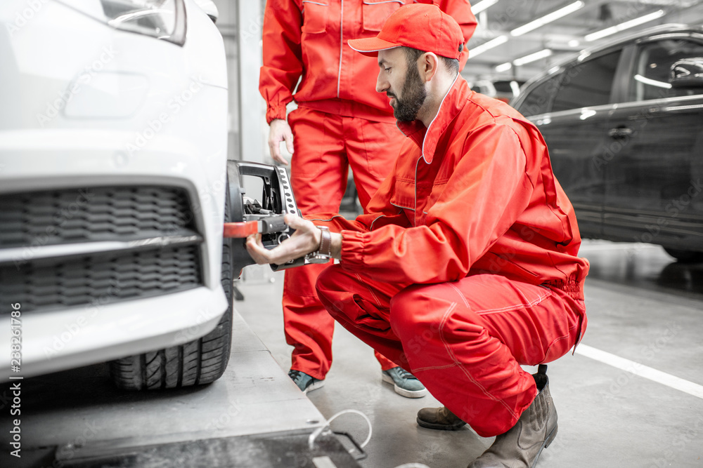 Two auto mechanics in red uniform fixing disk for wheel alignment on a luxury car at the car service
