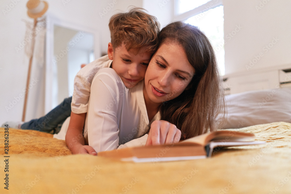 Smiling mother and son embracing and reading book together Smiling mother and son embracing and reading book together