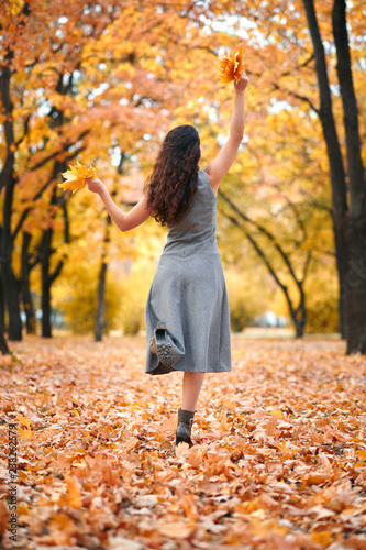 Pretty woman posing with bunch of maple's leaves in autumn park. Beautiful landscape at fall season.