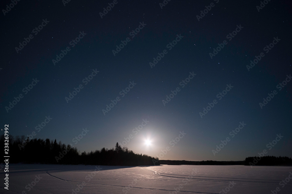 Moon rising over winter landscape at night.