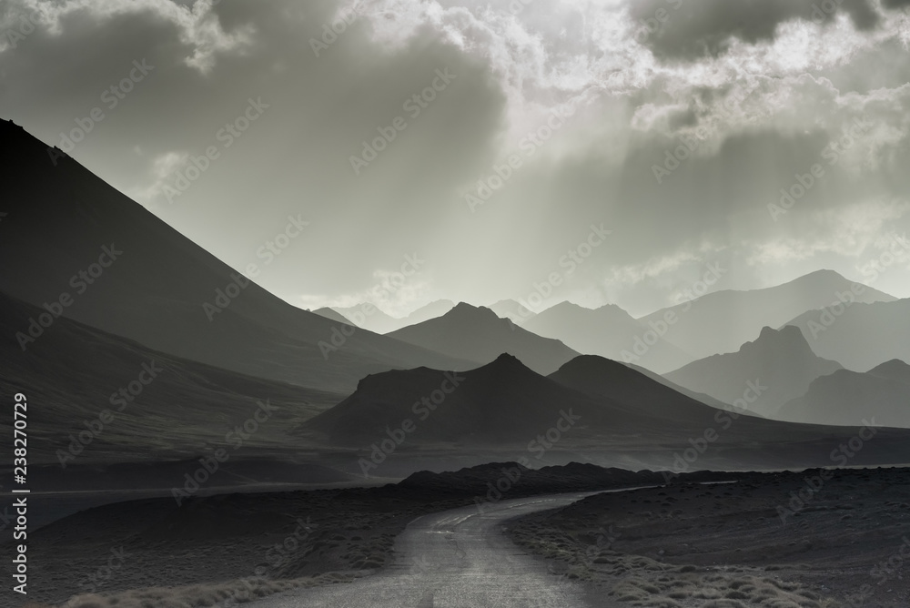 Fototapeta premium Monochrome landscape of layered mountains. Silhouettes of mountains in the setting sun. Black and white landscape. The road among the rocks.