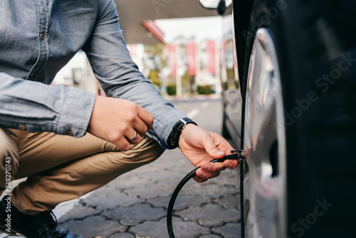 фотографія Close up of man crouching on the gas station and inflating tire.