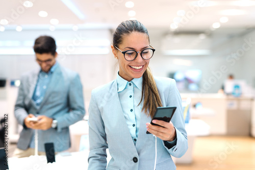 Young Caucasian woman dressed in suit trying out new smart phone. Tech store interior.