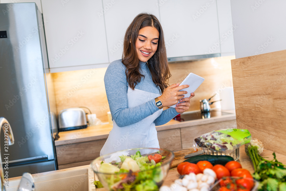 Woman In Kitchen Following Recipe On Digital Tablet