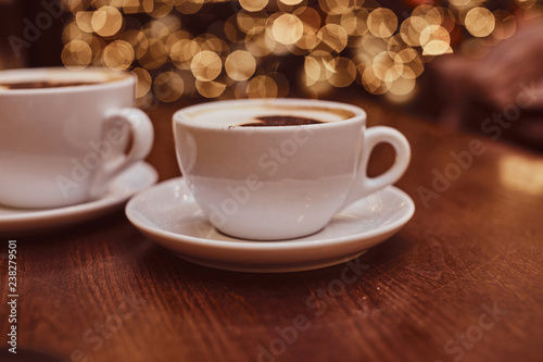 Two cups of hot coffee with art on the wooden table in a coffee shop, blur background with bokeh effect