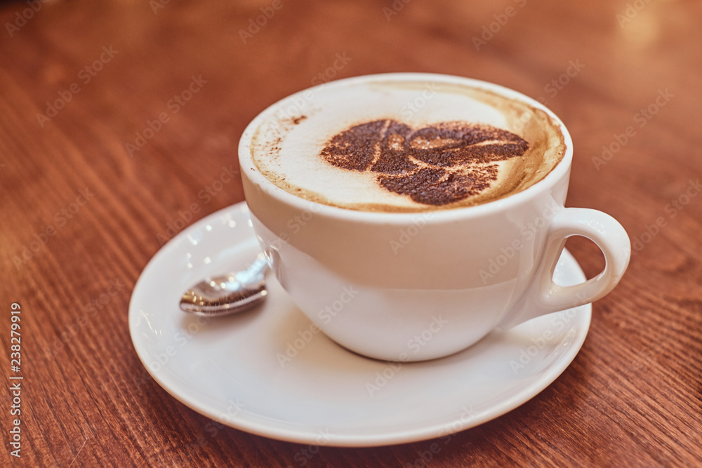 Hot coffee with art in a cup on the wooden table in a coffee shop, blur background with bokeh effect Hot coffee with art in a cup on the wooden table in a coffee shop, blur background with bokeh effect