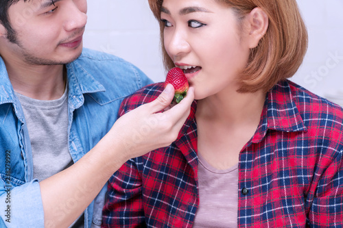 Healthy food concept. Attractive young couple holding and eating strawberries on breakfast in the kitchen at home.