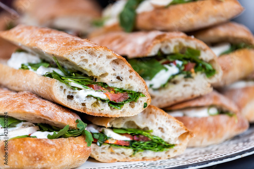 Closeup of fresh display of stacked pile of panini bread, mozzarella melted cheese, vegetarian italian tomatoes, basil lettuce in store, shop, cafe buffet catering sandwiches