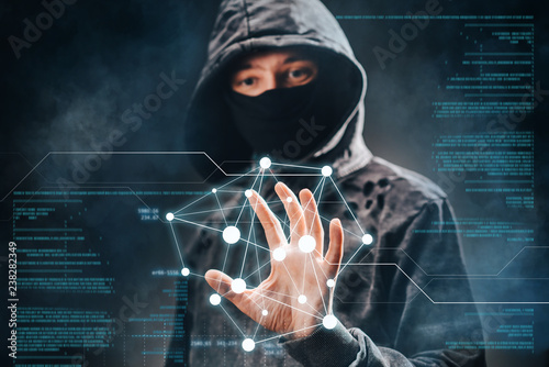 Cyber crime. Male hacker accessing to personal information. Hooded man with obscured face touching digital panel with mixed media and binary code. Virtual crime, cybersecurity concept. photo