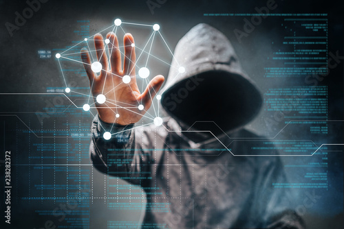 Cyber crime. Male hacker accessing to personal information. Hooded man with obscured face touching digital panel with mixed media and binary code. Virtual crime, cybersecurity concept. photo