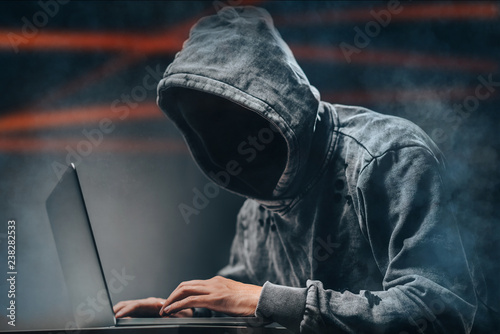 Cyber crime. Male hooded hacker with hidden face accessing to personal information on a computer in the dark. Technologal, cyber crime concept photo