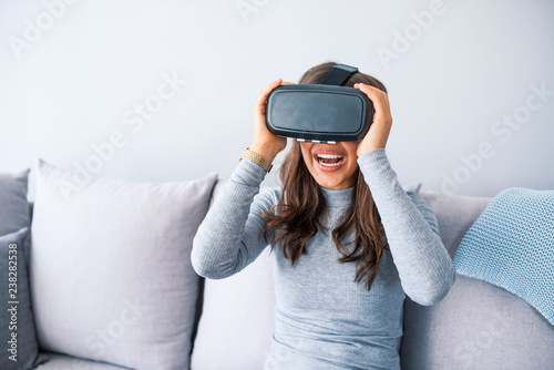 It is so real! Attractive young woman adjusting her VR headset and smiling while sitting on the sofa.