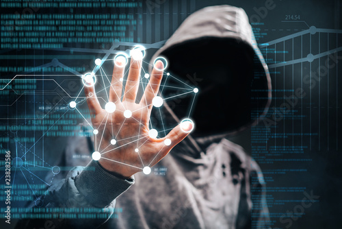 Cyber crime. Male hacker accessing to personal information. Hooded man with obscured face touching digital panel with mixed media and binary code. Virtual crime, cybersecurity concept. photo