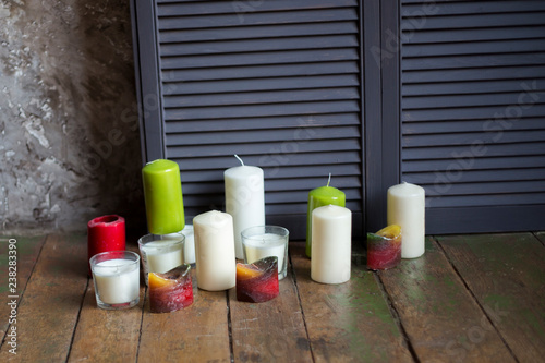 candles of different flowers and forms stand on a floor near a wall