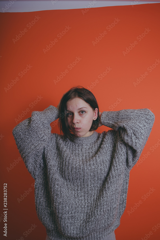 Young girl in warm grey sweater posing on orange background, woman with short haircut in knitted sweater, space for text Young girl in warm grey sweater posing on orange background, woman with short haircut in knitted sweater, space for text