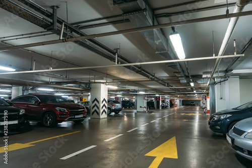Illuminated underground car parking interior under modern mall with lots of vehicles and arrows on floor