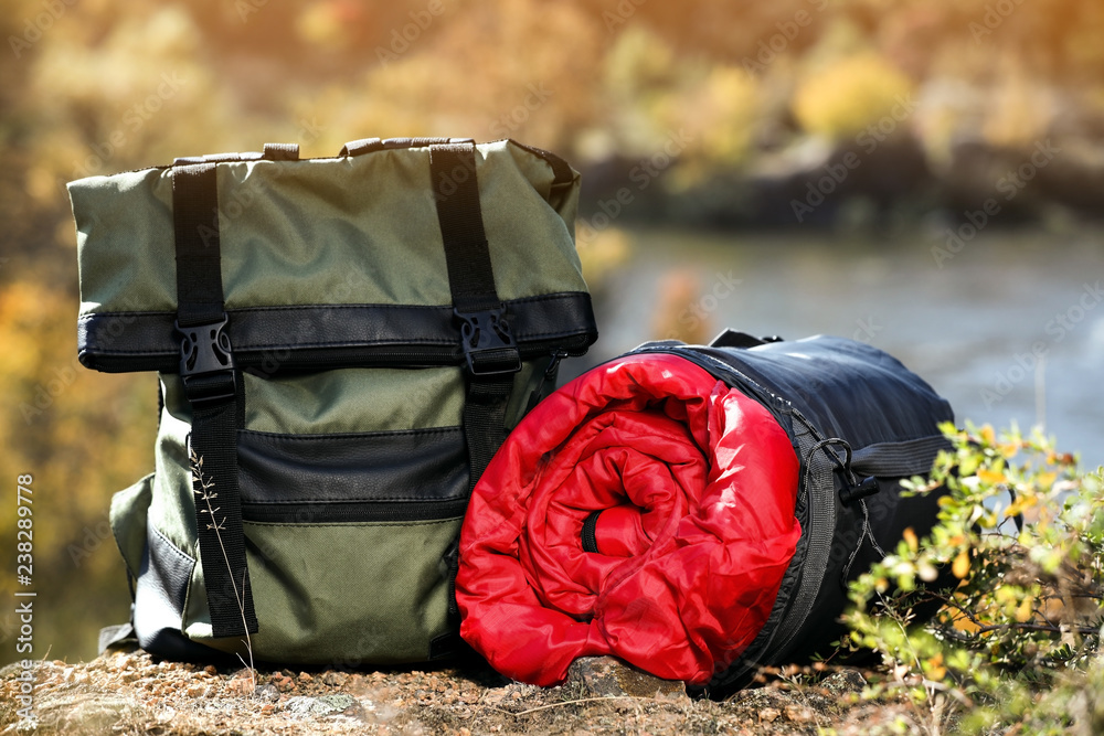 Backpack and sleeping bag on ground outdoors. Camping equipment - obrazy, fototapety, plakaty 