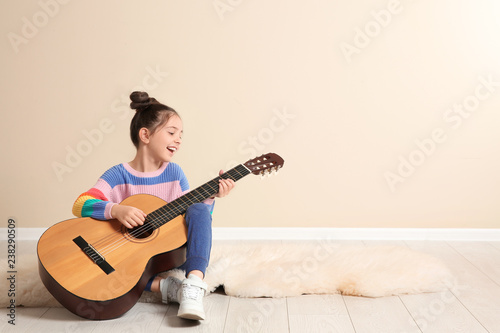Cute little girl playing guitar on floor in room. Space for text