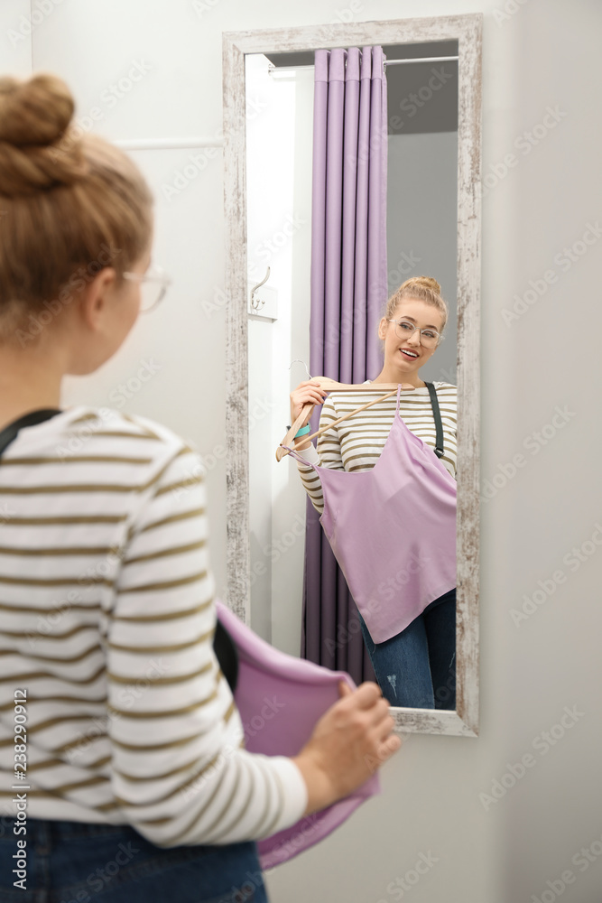 Young woman with clothes on hanger in dressing room. Fashion store