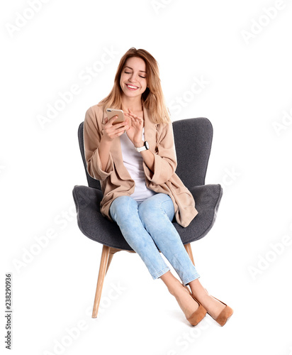 Young woman with smartphone sitting in armchair on white background