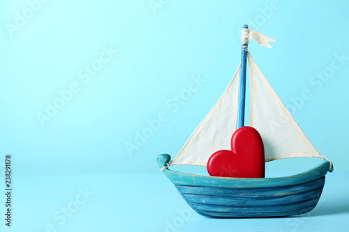 Toy ship with red decorative heart on color background. Space for text