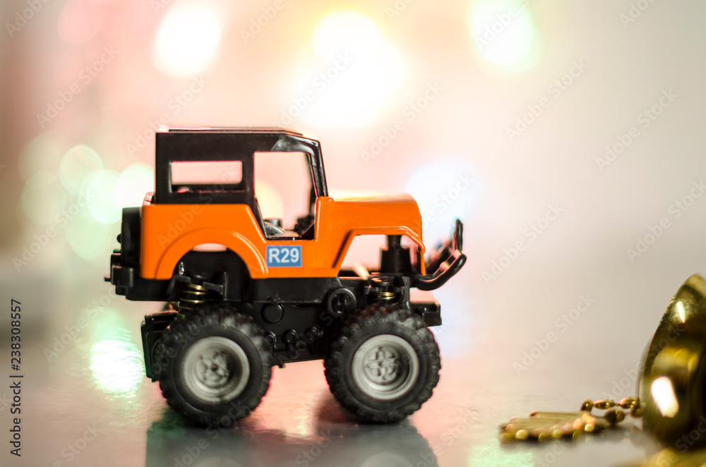 Plastic toy orange car against fairy lights. Toy car against blurred background. Cute little car Plastic toy orange car against fairy lights. Toy car against blurred background. Cute little car