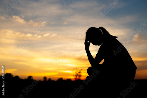 Silhouette of sad and depressed women sitting at walkway of park with sunset