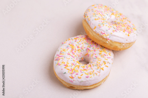 Two delicious vanilla donuts with sprinkle on light marble background
