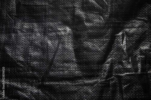 The texture of black crumpled polyethylene woven fabric. Abstract dark background of synthetic polypropylene or polyethylene (PP, PE) material which used as outdoor tarpaulin.