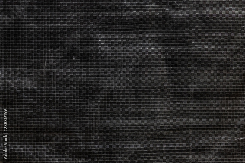 The texture of black polyethylene woven fabric. Abstract dark background of synthetic polypropylene or polyethylene (PP, PE) material which used as outdoor tarpaulin.