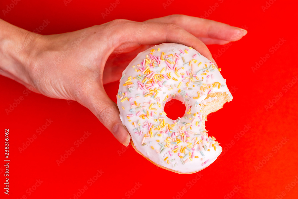 Bitten tasty vanilla donut with sprinkle in woman's hands