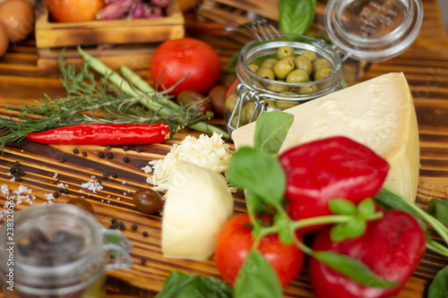 Close up cheese, peppers, green olives, tomatoes and spices. Food background, vegetable composition. Fresh ingredients for preparation salad, pizza, pasta on wooden table. Healthy diet and nutrition.